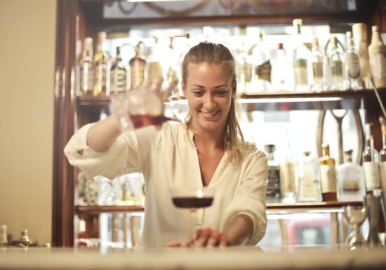 Bartender pouring a drink into a glass behind a bar.