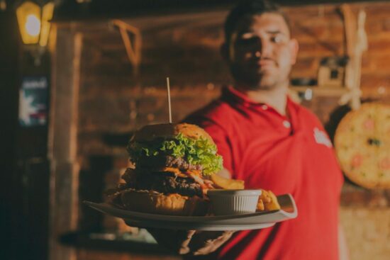 Server holding a large burger with fries on a plate