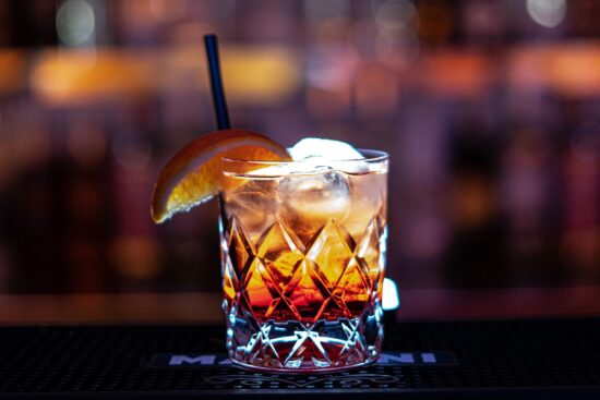 Old fashioned cocktail with ice, orange slice, and straw